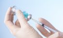 Hands using needle to extract vaccine from bottle