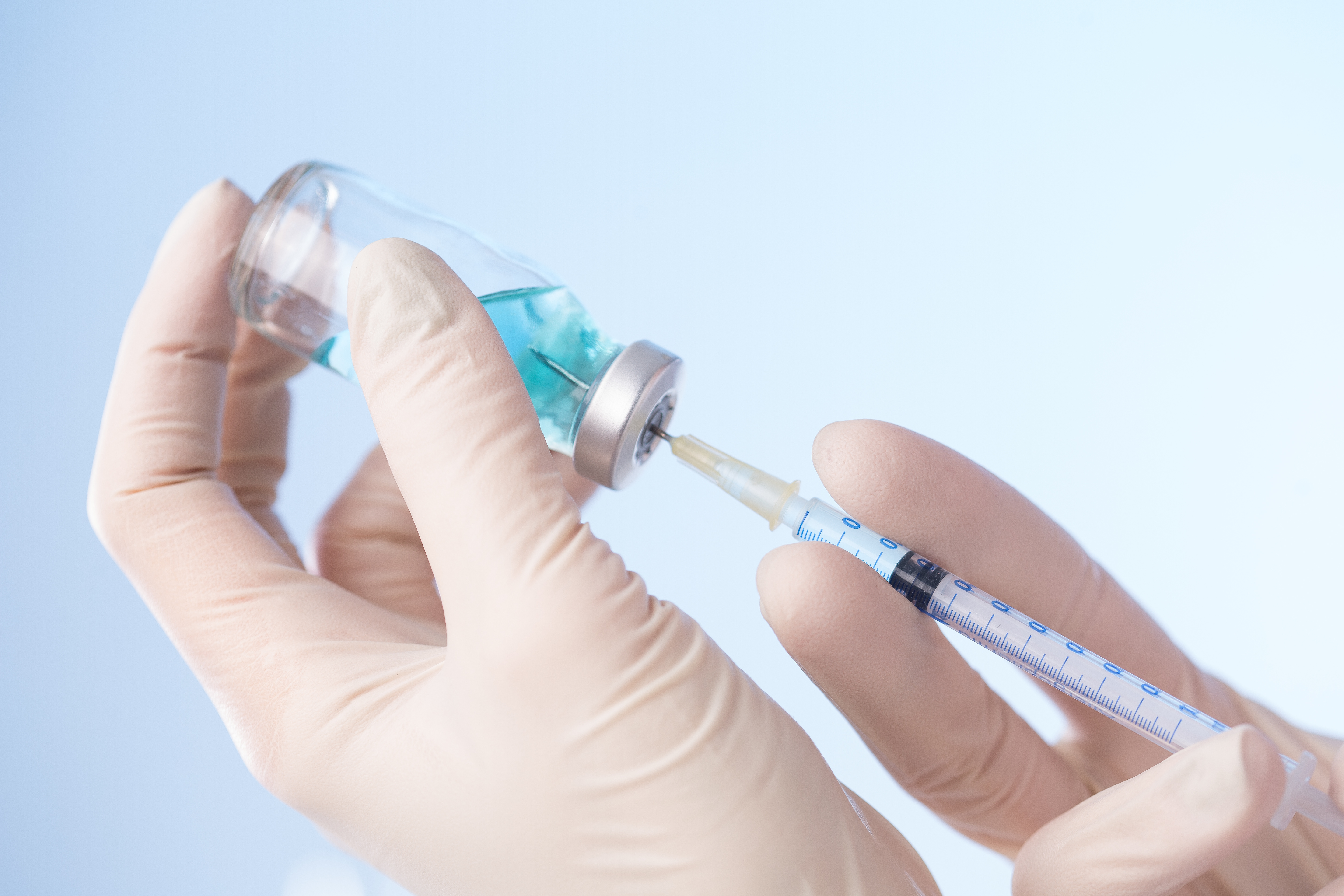 Hands using needle to extract vaccine from bottle